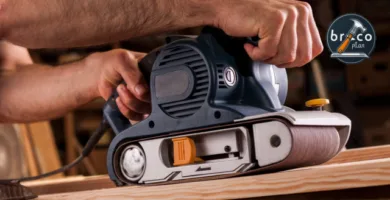 Hombre usando una lijadora de banda eléctrica sobre un tablero de madera en un taller, lijando la superficie con precisión.